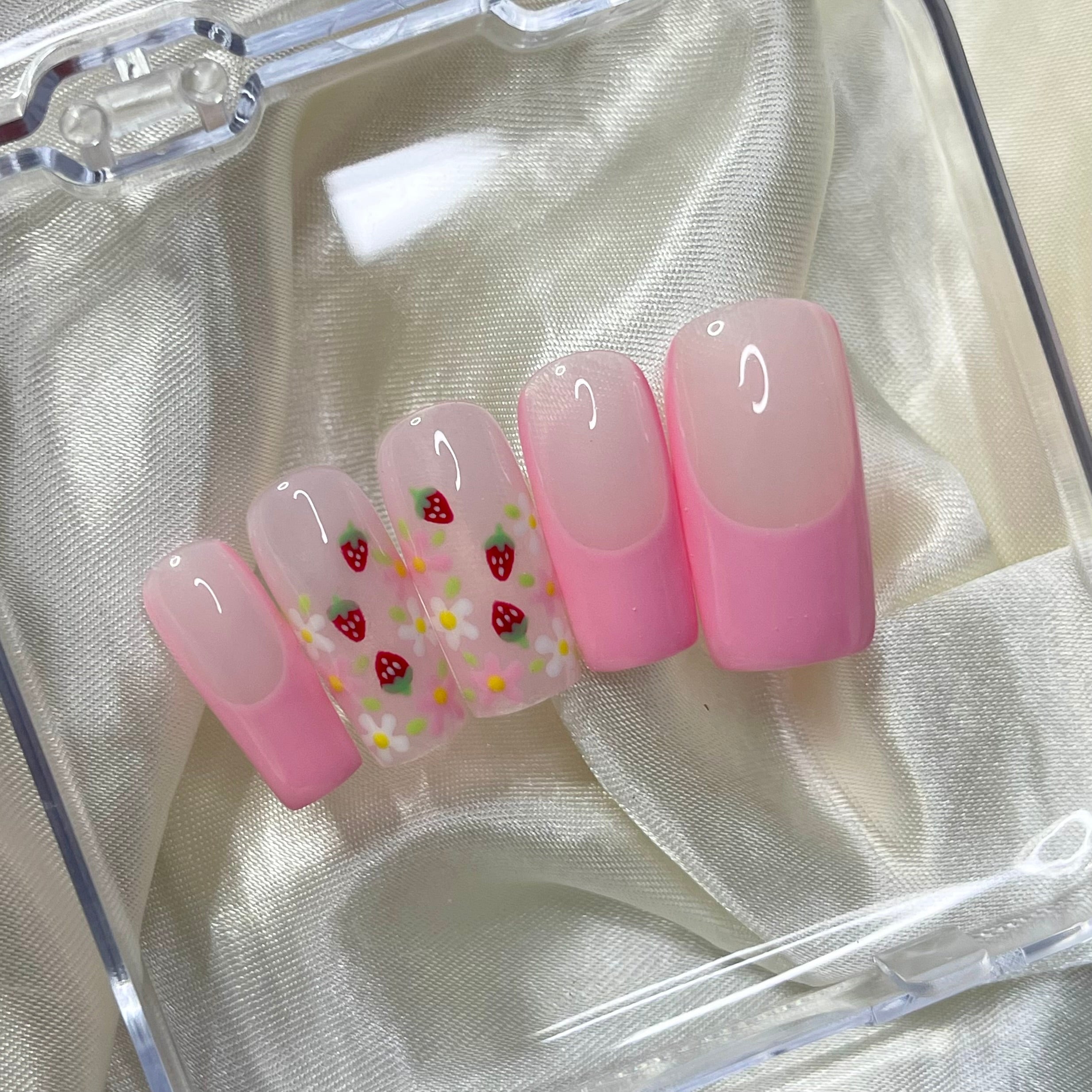 Strawberry Patch press-on nails feature rosy pink French tips, white and pink flowers, golden centres, hand-painted strawberries, and soft pinky nude bases for a fresh, fruity spring look.